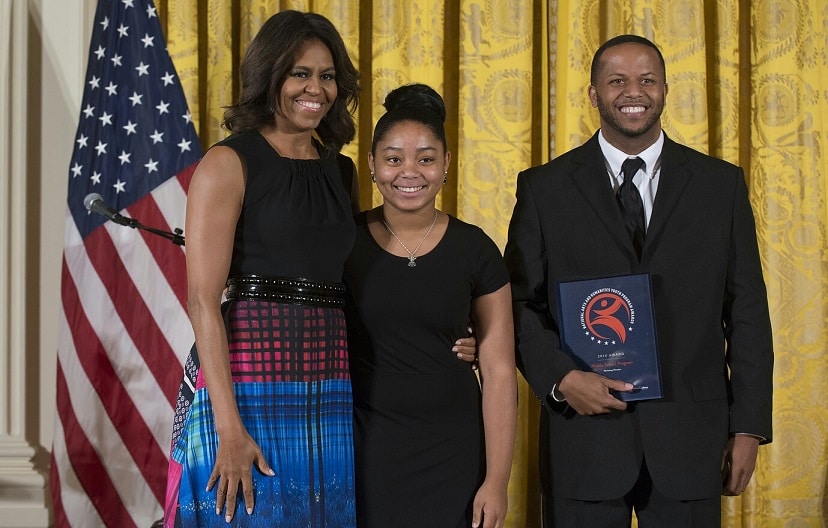 First Lady Michelle Obama presents the  2014 National Arts and Humanities Youth Program Award to student Brianna Burns and Workshop Houston Co-Director Reginald Hatter '03.
